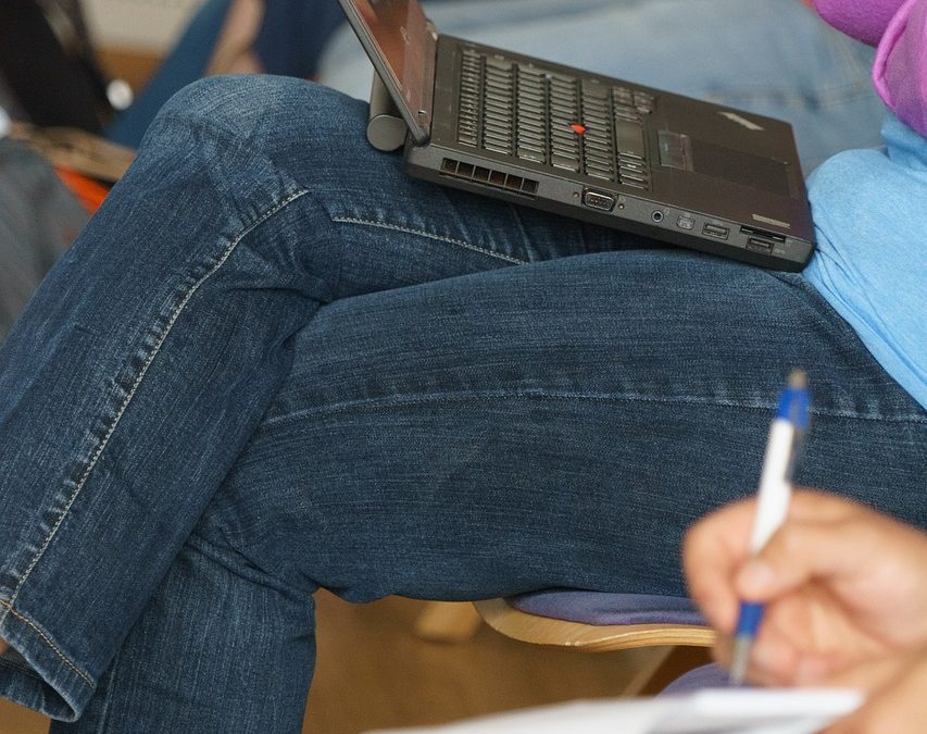 Person sitzt auf Stuhl hat einen aufgeklappten Laptop auf dem Schoß